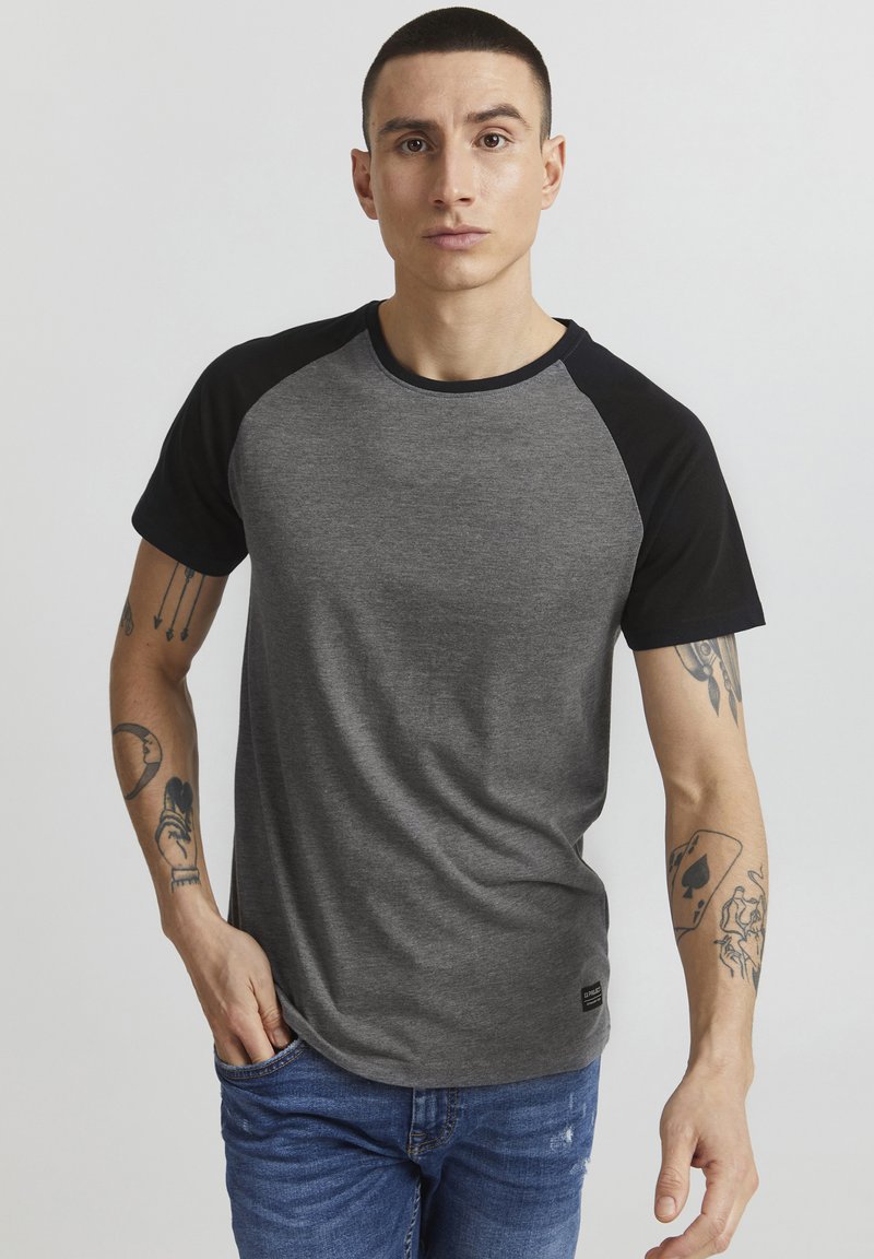 Camiseta raglán gris y negra hecha de tela suave, con cuello redondo y mangas cortas, con una sutil textura y detalle de logo en el dobladillo.