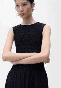 Abito nero senza maniche con corpino testurizzato e arricciato e gonna fluente. Presenta un collo rotondo e un tessuto morbido. Design minimalista.