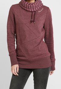 Sudadera burdeos con cuello alto a rayas, tela texturada, diseño de costuras diagonales y puños y dobladillo acanalados. Presenta detalles con cordón.