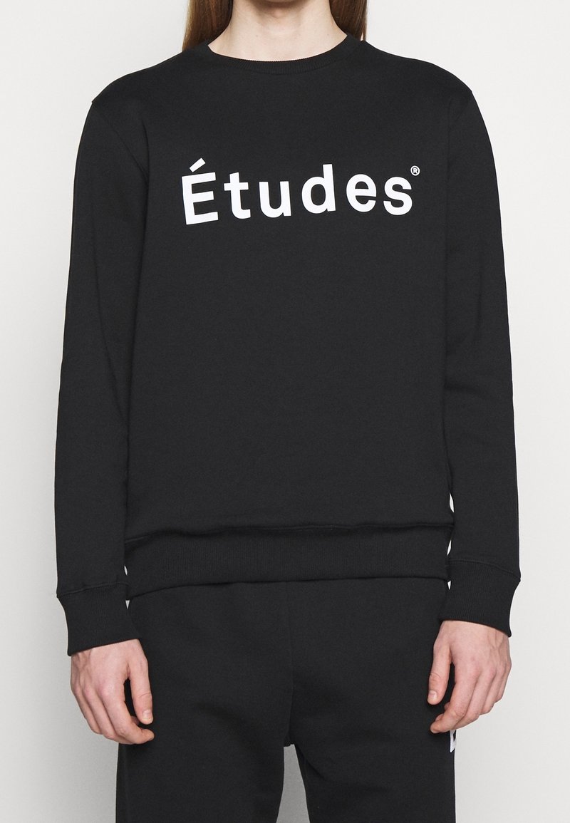 Sudadera negra de algodón, con cuello redondo y puños acanalados, y con un llamativo texto en blanco "Études" en la parte delantera.