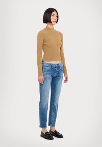 Haut long à manches longues en tricot côtelé beige associé à un jean bleu clair taille mi-haute. Des mocassins noirs avec un détail doré complètent la tenue.