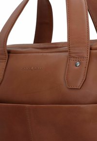 Braune Leder-Umhängetasche mit doppelten Griffen, die eine glatte Textur und dezente Branding-Details aufweist. Beinhaltet metallene Hardware-Elemente für Langlebigkeit.