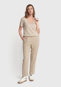 Beige kortærmet v-hals t-shirt i kombination med lysebeige skræddersyede bukser. Sneakers har en hvid overdel og en brun sål. Minimalistisk design.