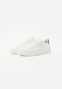 White sneakers with perforated design on the side, textured leather, flat rubber sole, and a blue accent on the heel.