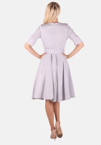 Helles graues Kleid mit kurzen Ärmeln, weißen Punkten, tailliertem Schnitt und vollem Rock, mit einem Gürtel in der Taille. Getragen mit nudefarbenen Absätzen.