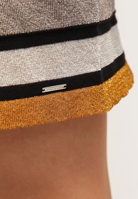 Jupe en maille avec des rayures métalliques argentées, noires et dorées, un ourlet texturé doré et une étiquette argentée portant la mention « DIESEL ».