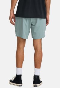 Pantalones cortos atléticos de color verde claro con una cinturilla elástica, textura suave y bolsillos laterales, combinados con zapatillas altas negras y calcetines blancos.