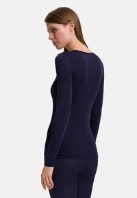 Marinblå långärmad topp med en figurnära design, mjuk textur och rundad halsringning, med sömlös konstruktion för komfort och mångsidighet.