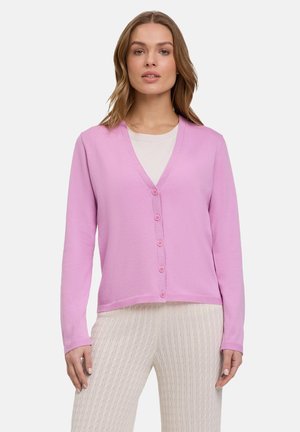 Cardigan rosa chiaro con scollo a V, chiusura a bottoni e maniche lunghe, abbinato a pantaloni crema strutturati. Tessuto morbido, vestibilità rilassata.