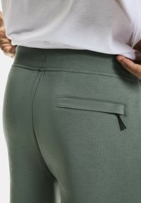 Groene joggingbroek van zacht materiaal, met een achterzak met een gestikte flap en een zwarte trekkoordaccent. Eenvoudig ontwerp.