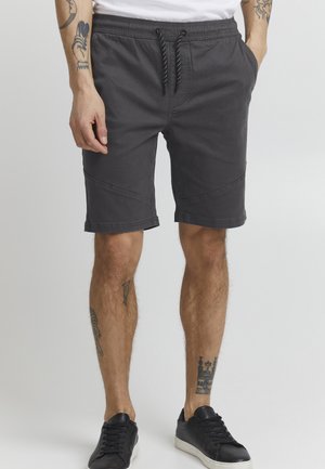 Gray cotton shorts with an elastic waistband, drawstring closure, side pockets, and front seam detailing, paired with black sneakers.