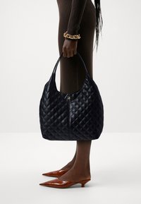 Czarna pikowana torba hobo ze skóry z pojedynczym uchwytem i zamkiem błyskawicznym; posiada mały srebrny detal metalowy.