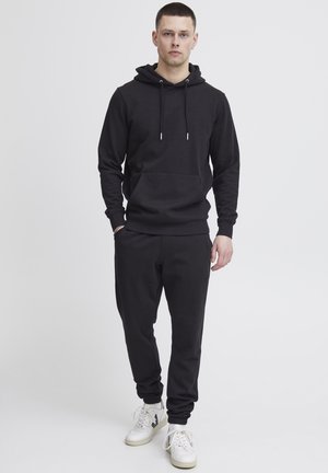 Svart hoodie med ficka fram och justerbara dragband, tillsammans med matchande svarta sweatpants, båda i ett mjukt, texturerat tyg.