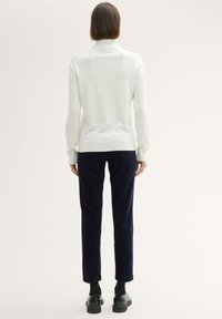 Vit ribbad polotröja kombinerad med mörkblå smalt skurna manchesterbyxor. Outfiten har långa ärmar och en figurnära silhuett.