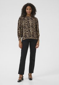 Leopard-print long-sleeve top in beige and black, paired with black straight-leg pants and black block-heeled shoes.