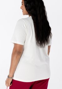 Witte t-shirt met korte mouwen en een ronde hals, met een gladde textuur en een losse pasvorm, gecombineerd met dieprode broek, wat casual kleding toont.