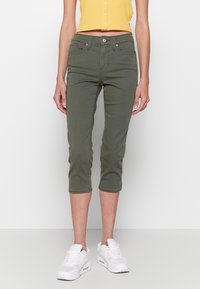 Oliwkowe, krótkie dżinsy o dopasowanym kroju, wykonane z miękkiego materiału, z zapięciem na guzik i paskiem. Noszone z białymi trampkami.