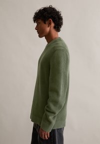 Pulover verde tricotat cu textură rib, decolteu rotund și mâneci lungi. Are un croi lejer și fante laterale la tiv.