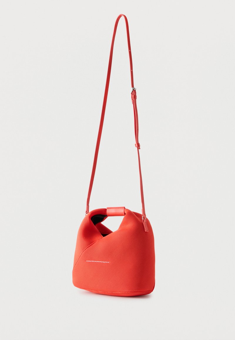 Sac à main rouge texturé avec une longue bandoulière ajustable et une courte poignée, présenté sur un fond clair uni.