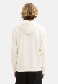 Lichtbeige hoodie met een zachte textuur, voorzien van een capuchon, geribbelde manchetten en zoom. De achterkant is eenvoudig zonder patronen of grafische elementen.