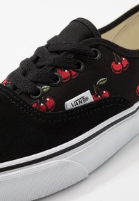 Černé tenisky Vans s jasně červenou výšivkou třešní, černými tkaničkami a bílou gumovou podrážkou s jemným černým pruhem.