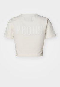 Krämfärgad kortärmad t-shirt av bomull med korta ärmar, försedda med upphöjd text "PEQUS" på baksidan. Slät textur och enkel design.