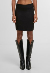 Černá pletená sukně s přiléhavým střihem, žebrovaným páskem a lemem. Vytvořeno ve spojení s vysokými černými koženými botami na špičatou špičku, které mají široké otevření.
