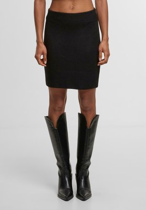 Jupe noire en tricot au design ajusté, avec une taille côtelée et un ourlet. Associée à des bottes noires en cuir à bout pointu et à ouverture large.