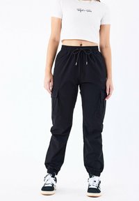 Sorte cargo bukser med elastiske manchetter, snoreliv og sidelommer. Parret med sort-hvide sneakers og en kort hvid t-shirt.
