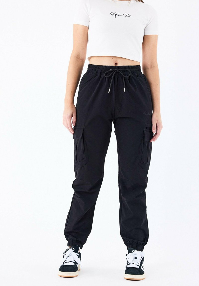 Sorte cargo bukser med elastiske manchetter, snoreliv og sidelommer. Parret med sort-hvide sneakers og en kort hvid t-shirt.