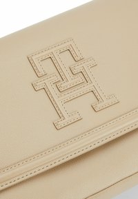 Beige læder clutch med tekstureret overflade, der har et fremtrædende præget logo-design. Kompakt, rektangulær form med stikninger.