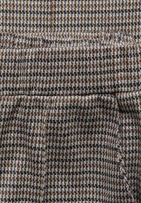 Hnědo-krémová tkanina s vzorem houndstooth a texturovaným povrchem, s jemnými modrými a černými niti protkávanými po celé ploše.