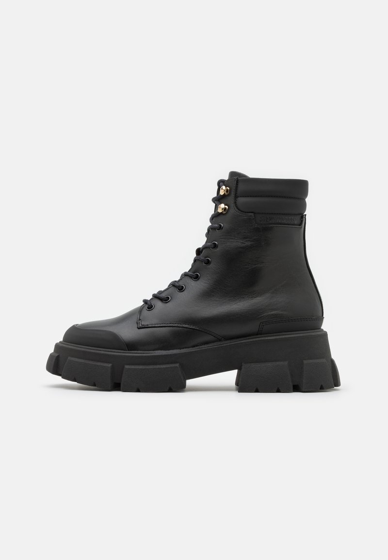 Botte de combat en cuir noir à lacets avec col rembourré à la cheville et semelle épaisse à relief, vue de côté sur fond uni.