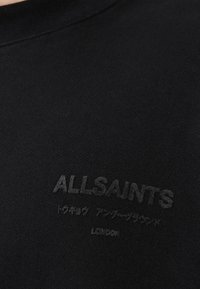 Μαύρο φούτερ κατασκευασμένο από υφασμάτινη υφή. Διαθέτει διακριτικές λογοτύπες σε τον ικό χρώμα με τα γράμματα "ALLSAINTS" και "LONDON" τυπωμένα με ματ τελείωμα.