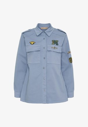 Lyseblå langærmet skjorte med knaplukning, to brystlommer og broderet bi samt mærker på brystet og ærmerne.