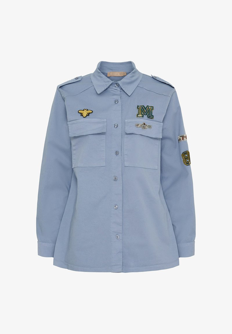 Lyseblå langærmet skjorte med knaplukning, to brystlommer og broderet bi samt mærker på brystet og ærmerne.