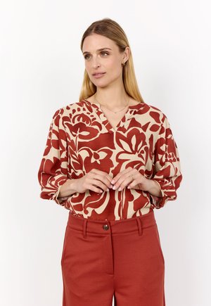 Red and beige floral printed blouse with a v-neck and puffed sleeves, paired with rust-colored tailored pants.