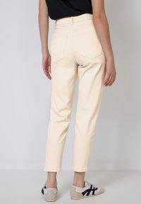 Jeans de corte recto de talle alto color crema, con dos bolsillos traseros y dobladillo vuelto. Combinados con zapatillas blancas y negras.