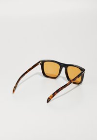 Schildpatt-Sonnenbrille mit bernsteinfarbenen Gläsern, quadratischen Rahmen und schlanken Bügeln, die nahe den Scharnieren eine subtile goldene Akzentuierung aufweisen.