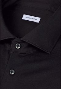 Gros plan d'un col de chemise noire à boutons et de deux boutons avec une étiquette blanche à l'intérieur indiquant "seidensticker."