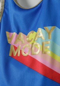 Débardeur bleu côtelé avec le texte doré "VACAY MODE" et des rayures diagonales multicolores en rouge, rose, jaune et accents bleu clair.
