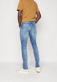 Ljusblå denimjeans med slim fit, femficksdesign och subtila slitningar, kombinerade med en brun kortärmad skjorta och beiga sneakers.