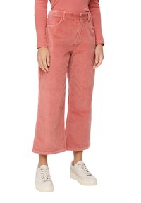 Woman wearing high-waist, wide-leg pink corduroy pants with front pockets, paired with cream platform sneakers and a matching pink long-sleeve top.