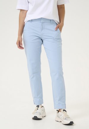 Pantalones ajustados de color azul claro, con bolsillos y una textura suave, combinados con zapatillas blancas y beiges.
