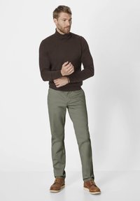 Brauner Rollkragenpullover, grüne Hose und braune Lederstiefel. Der Pullover hat einen taillierten Schnitt mit Rippbündchen, die Hose hat eine glatte Textur und einen geraden Schnitt.