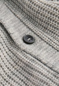 Gestrickte graue Jacke aus Stoff mit einem strukturierten Muster, die einen schwarzen Kunststoffknopf mit vier Löchern im Bereich des Kragens hat.