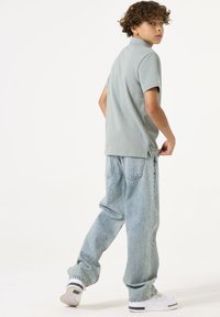 Polo vert clair associé à un jean en denim bleu ample. Les jeans présentent une décoloration et des détails de couture subtils. Des baskets blanches complètent la tenue.