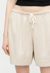 Shorts en lin beige avec taille élastique et cordon de serrage à l'avant, portés avec un haut court noir, visibles de la taille jusqu'à la mi-cuisse.