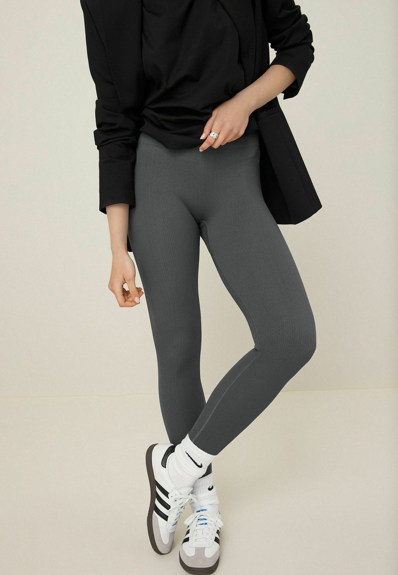 Szürke bordás leggings fekete oversized pólóval és fehér alacsony szárú sportcipővel párosítva, fekete csíkokkal és fehér zoknikkal.