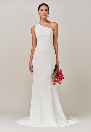 Hvid, halterneck kjole med et tætsiddende liv og en flodende nederdel. Glat stof, minimale sømme, parret med en buket af lyserøde blomster.